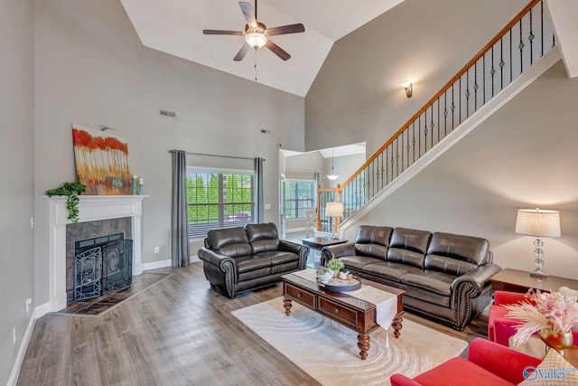 living area with ceiling fan, stairs, high vaulted ceiling, wood finished floors, and a tile fireplace