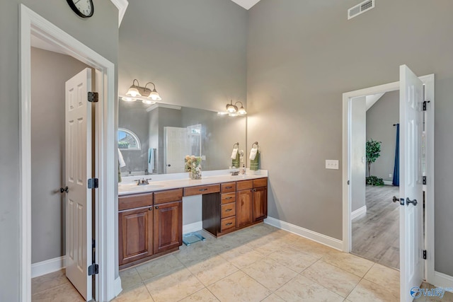 bathroom featuring double vanity, a sink, visible vents, baseboards, and a towering ceiling