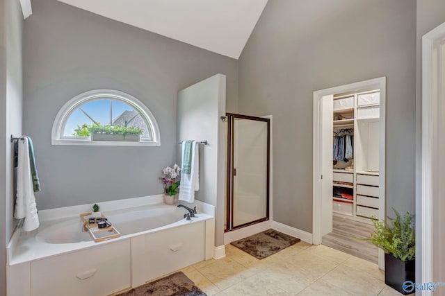 bathroom with lofted ceiling, a spacious closet, a shower stall, baseboards, and a bath