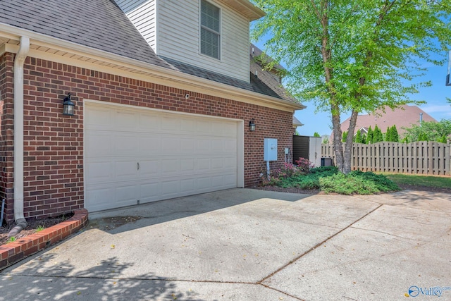 view of home's exterior with brick siding, fence, a garage, concrete driveway, and roof with shingles