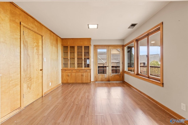 interior space with french doors, light hardwood / wood-style floors, and wood walls