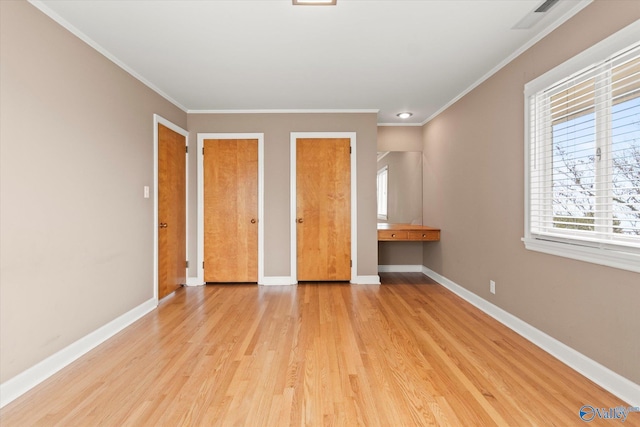 unfurnished bedroom with multiple closets, light hardwood / wood-style flooring, and ornamental molding