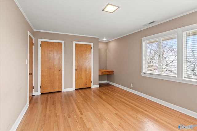 unfurnished bedroom featuring crown molding, light hardwood / wood-style floors, and two closets