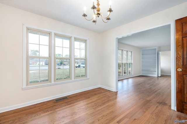 unfurnished dining area featuring an inviting chandelier, hardwood / wood-style floors, and built in features