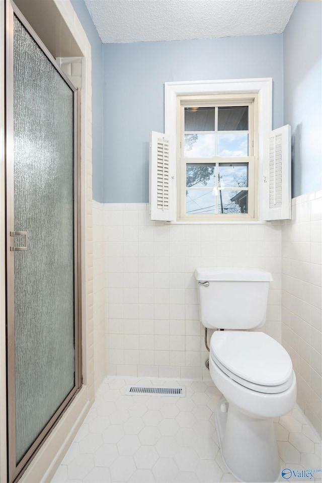 bathroom featuring a shower with door, tile walls, tile patterned flooring, a textured ceiling, and toilet