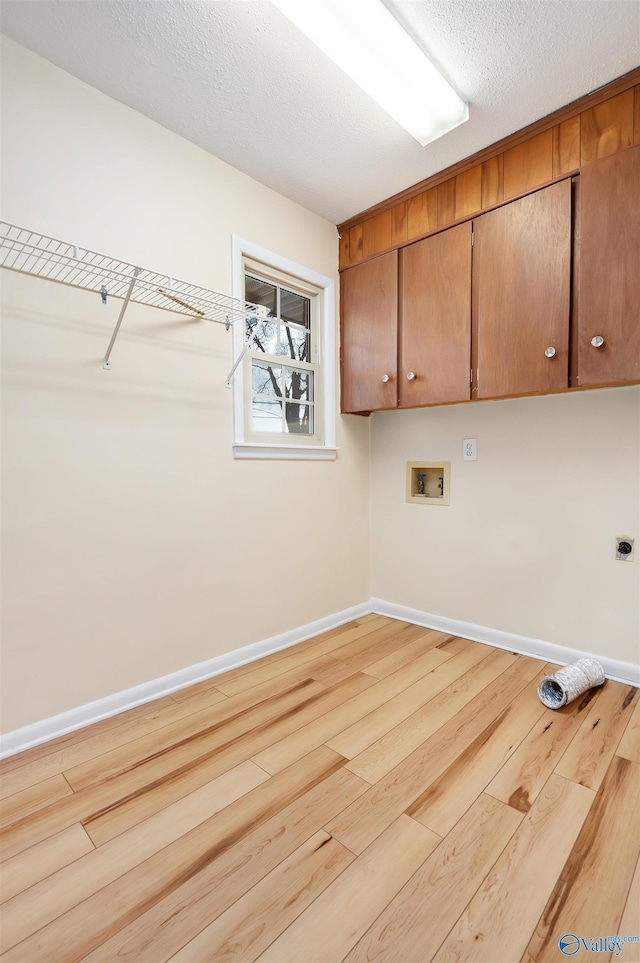 clothes washing area featuring cabinets, hookup for a washing machine, electric dryer hookup, a textured ceiling, and light hardwood / wood-style flooring