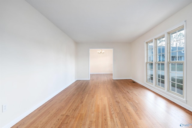 spare room with a chandelier and light wood-type flooring