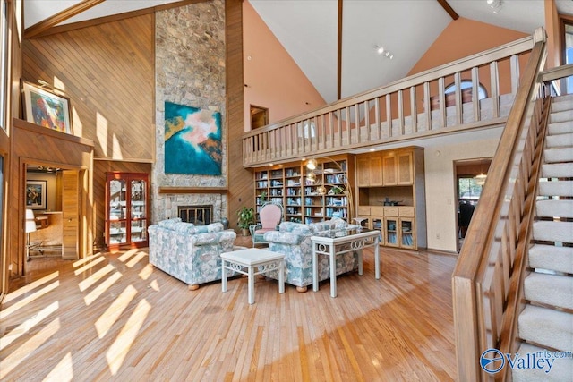 living room featuring light hardwood / wood-style floors, high vaulted ceiling, wooden walls, and a stone fireplace