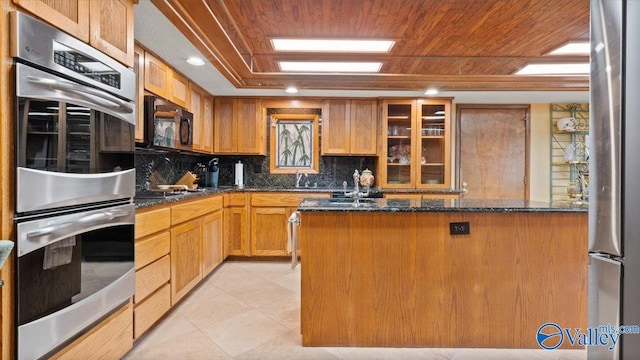 kitchen featuring dark stone countertops, backsplash, wood ceiling, double oven, and a kitchen island