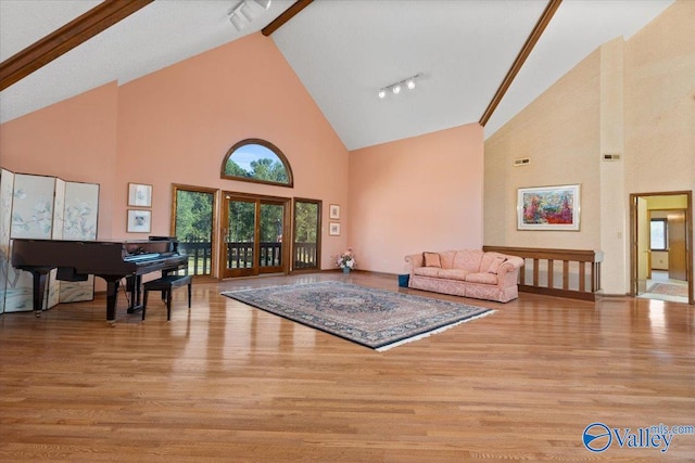 living room with beam ceiling, high vaulted ceiling, track lighting, and light hardwood / wood-style floors