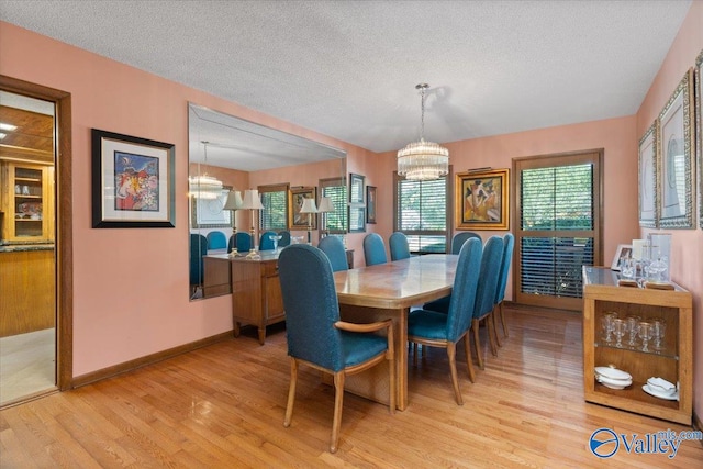 dining area featuring a textured ceiling, a notable chandelier, and light wood-type flooring