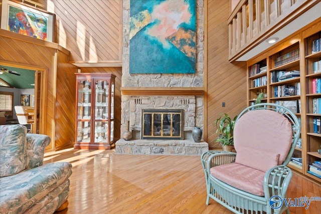 living room with a fireplace, hardwood / wood-style floors, built in shelves, wooden walls, and ceiling fan