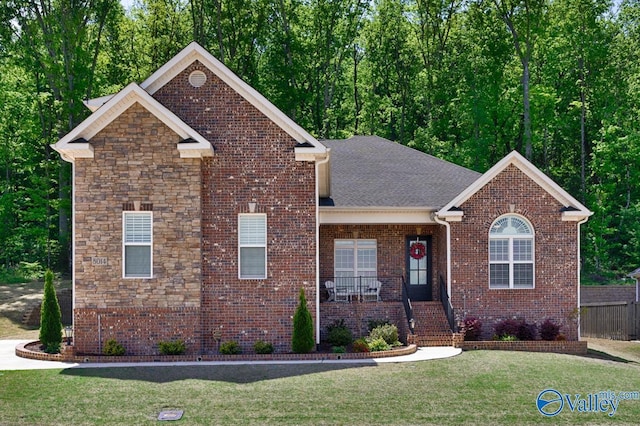 view of front of house with a porch, a front lawn, roof with shingles, and brick siding