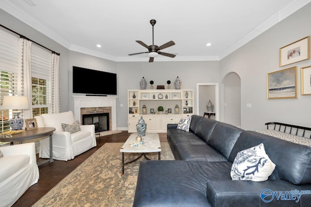 living room featuring ceiling fan, arched walkways, ornamental molding, and a stone fireplace