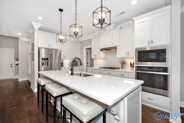 kitchen with under cabinet range hood, stainless steel appliances, visible vents, a sink, and a notable chandelier