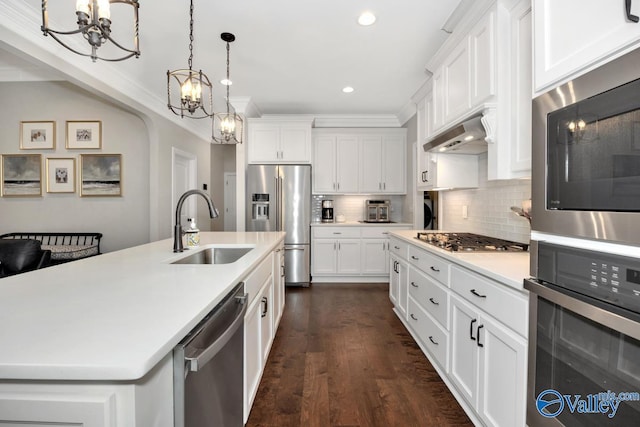 kitchen featuring dark wood-style floors, under cabinet range hood, stainless steel appliances, a sink, and a chandelier