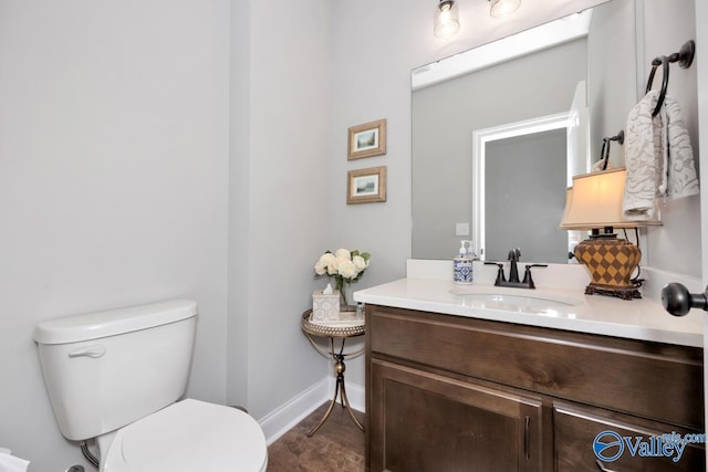 half bath featuring toilet, vanity, and baseboards