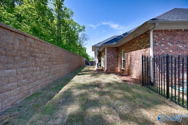 view of side of home featuring brick siding, a lawn, a shingled roof, and a fenced backyard