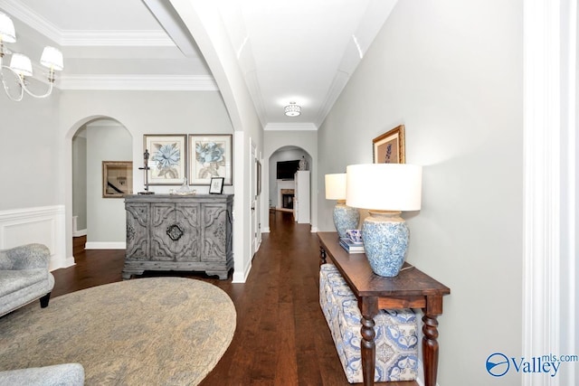 corridor featuring arched walkways, baseboards, crown molding, and dark wood-type flooring