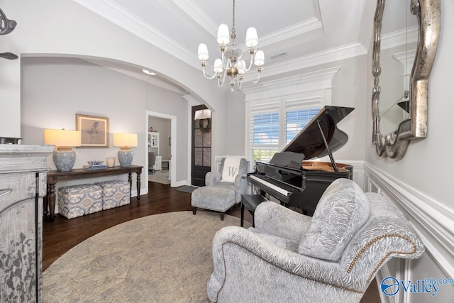living area with crown molding, wood finished floors, arched walkways, a tray ceiling, and a notable chandelier