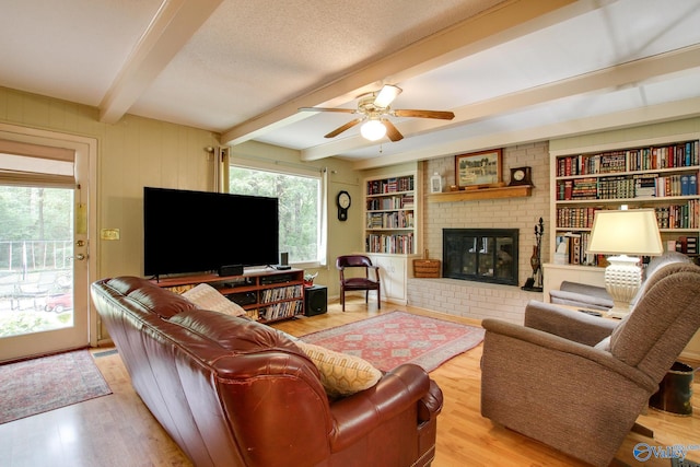 living room featuring a fireplace, light wood-type flooring, a textured ceiling, ceiling fan, and beam ceiling