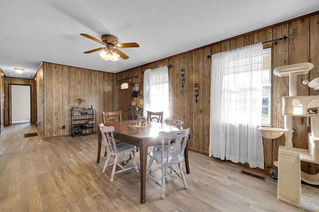 dining area featuring ceiling fan, light hardwood / wood-style floors, a textured ceiling, and wooden walls