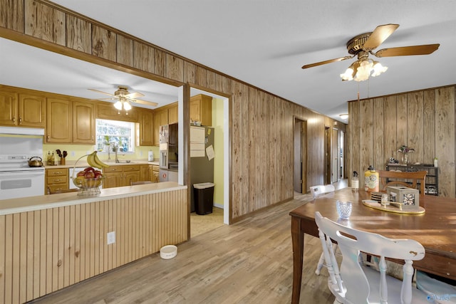 kitchen with white range oven, kitchen peninsula, wooden walls, and light wood-type flooring