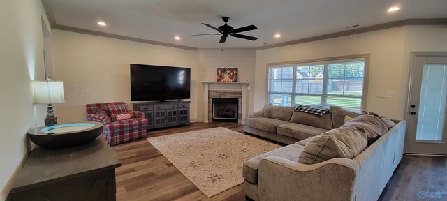 living room with crown molding, ceiling fan, hardwood / wood-style flooring, and a stone fireplace