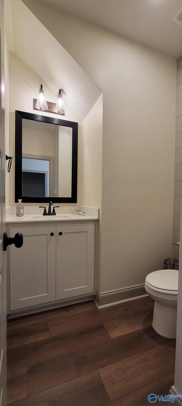 bathroom featuring wood-type flooring, lofted ceiling, vanity, and toilet