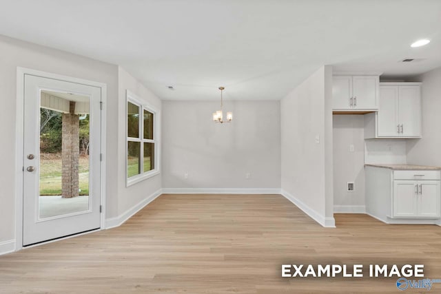 unfurnished dining area featuring light wood-type flooring, plenty of natural light, and a chandelier