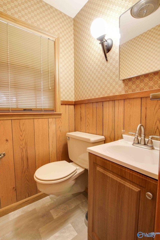 bathroom with vanity, wood walls, and toilet