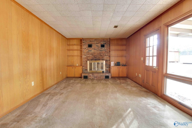 unfurnished living room with a brick fireplace, light colored carpet, built in features, and wooden walls