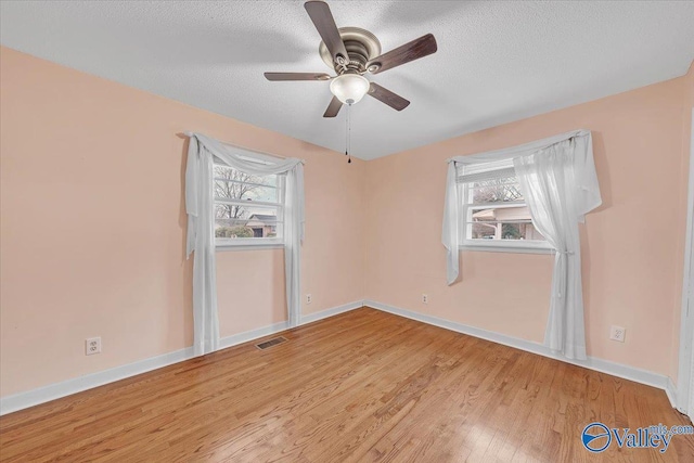 spare room with visible vents, a textured ceiling, baseboards, and wood finished floors