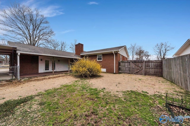 rear view of house featuring a gate, brick siding, a chimney, and a fenced backyard