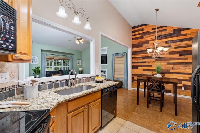 kitchen featuring lofted ceiling, wooden walls, black appliances, ceiling fan with notable chandelier, and light hardwood / wood-style floors