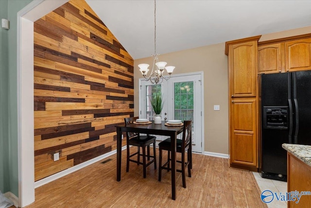 dining room featuring an inviting chandelier, wooden walls, vaulted ceiling, and light hardwood / wood-style flooring