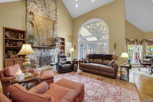 living room featuring high vaulted ceiling, light hardwood / wood-style floors, and a stone fireplace