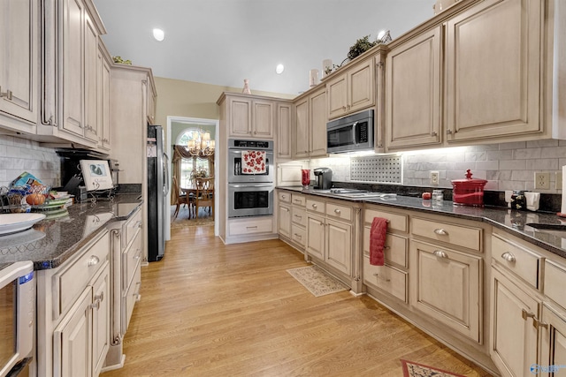 kitchen featuring light wood-type flooring, dark stone counters, tasteful backsplash, light brown cabinetry, and stainless steel appliances