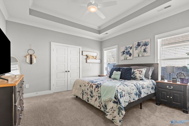 carpeted bedroom featuring ceiling fan, a closet, crown molding, and a tray ceiling