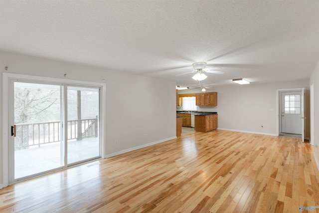 unfurnished living room with ceiling fan, a healthy amount of sunlight, a textured ceiling, and light wood-type flooring