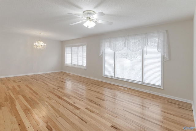 empty room with ceiling fan with notable chandelier, light hardwood / wood-style flooring, and a textured ceiling