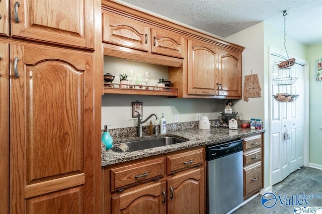 kitchen with a sink, a textured ceiling, stainless steel dishwasher, brown cabinetry, and dark stone countertops