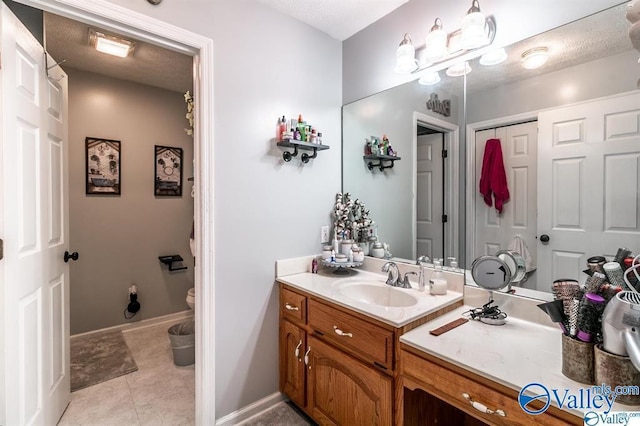 bathroom with vanity, toilet, baseboards, a textured ceiling, and tile patterned floors