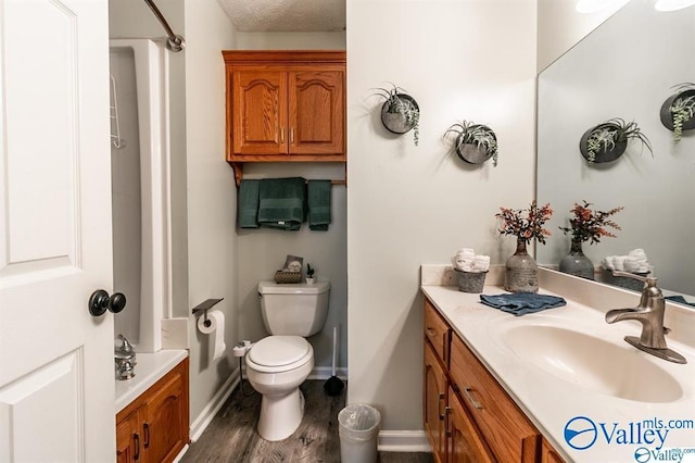 full bath featuring toilet, vanity, wood finished floors, a textured ceiling, and baseboards