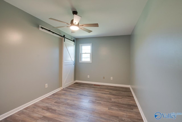 empty room featuring hardwood / wood-style flooring, a barn door, and ceiling fan