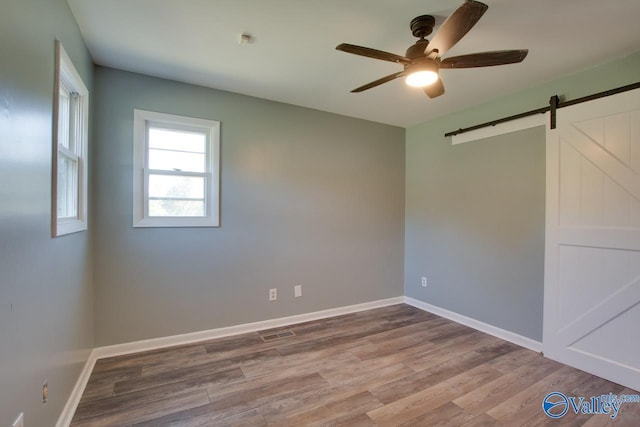 unfurnished room featuring hardwood / wood-style floors, a barn door, and ceiling fan