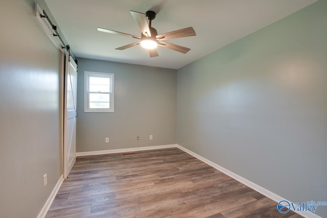 empty room featuring hardwood / wood-style floors, a barn door, and ceiling fan