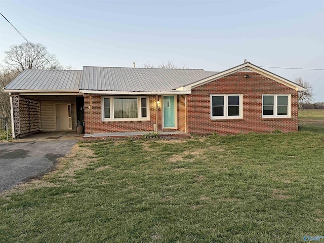 ranch-style house featuring driveway, a carport, a front yard, metal roof, and brick siding