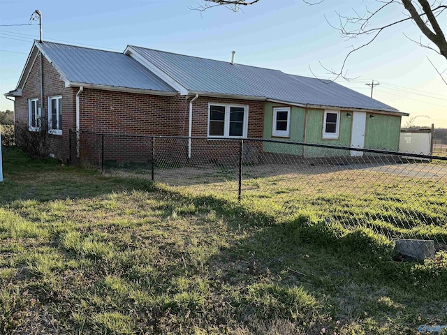 exterior space featuring metal roof, brick siding, a lawn, and fence