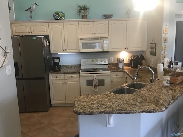 kitchen featuring a breakfast bar, a sink, dark stone countertops, white appliances, and a peninsula